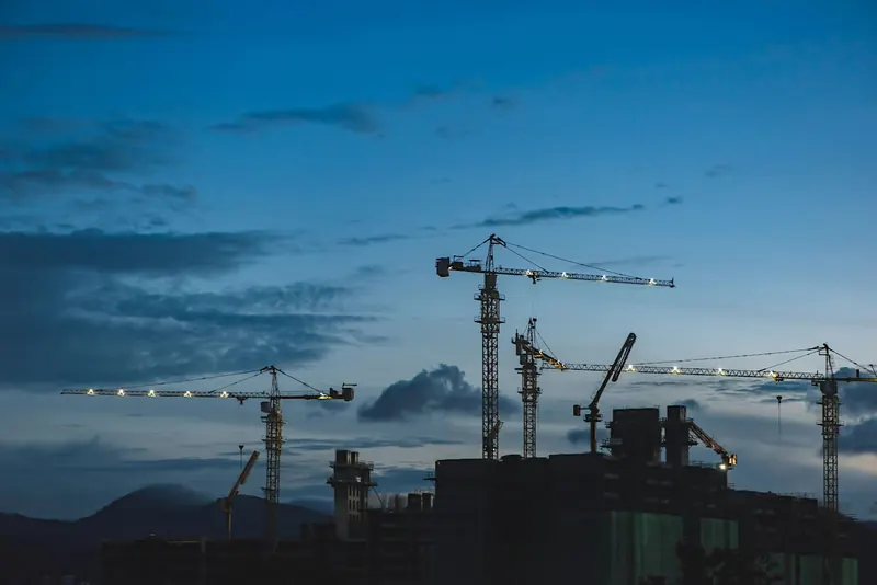 Tower cranes lit up over a building site at dusk