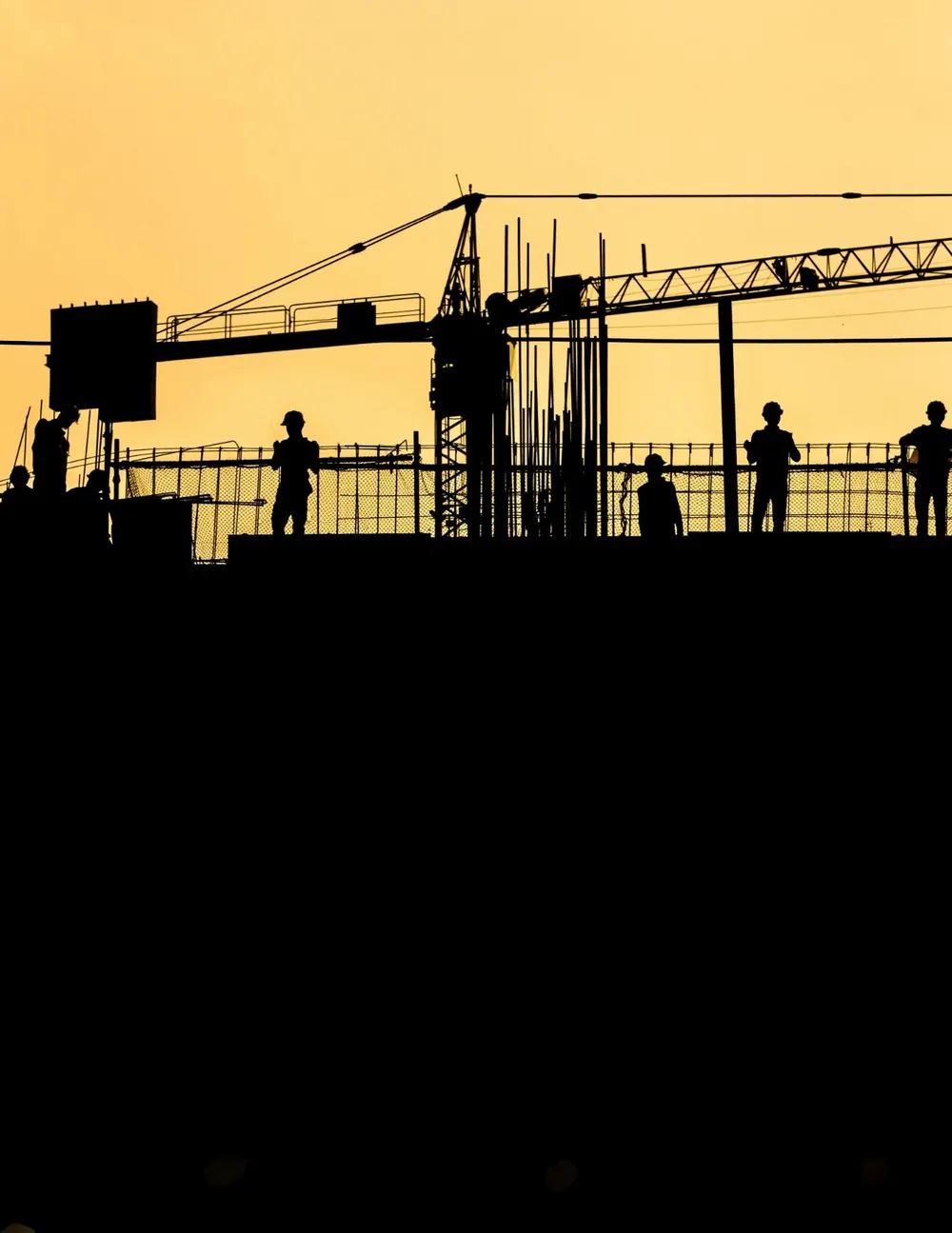 Construction workers in silhouette on a building site at sunset, a tower crane behind them
