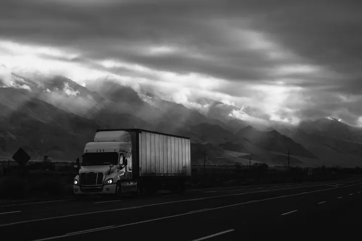 Poids lourd sur une autoroute au pied des montagnes, sous un ciel chargé