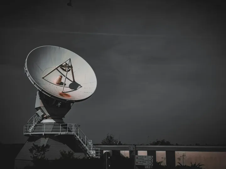 A large satellite ground station dish on its tower under a dark grey sky