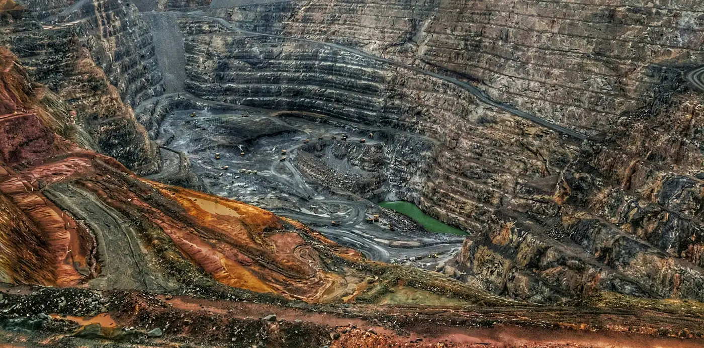Une mine à ciel ouvert sous un ciel gris : gradins, pistes de roulage et camions au fond de la fosse